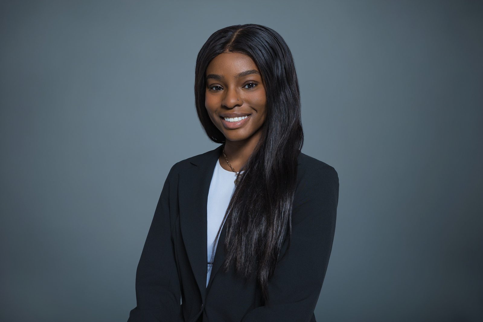 Studio headshot of a smiling woman in a black blazer against a gray backdrop