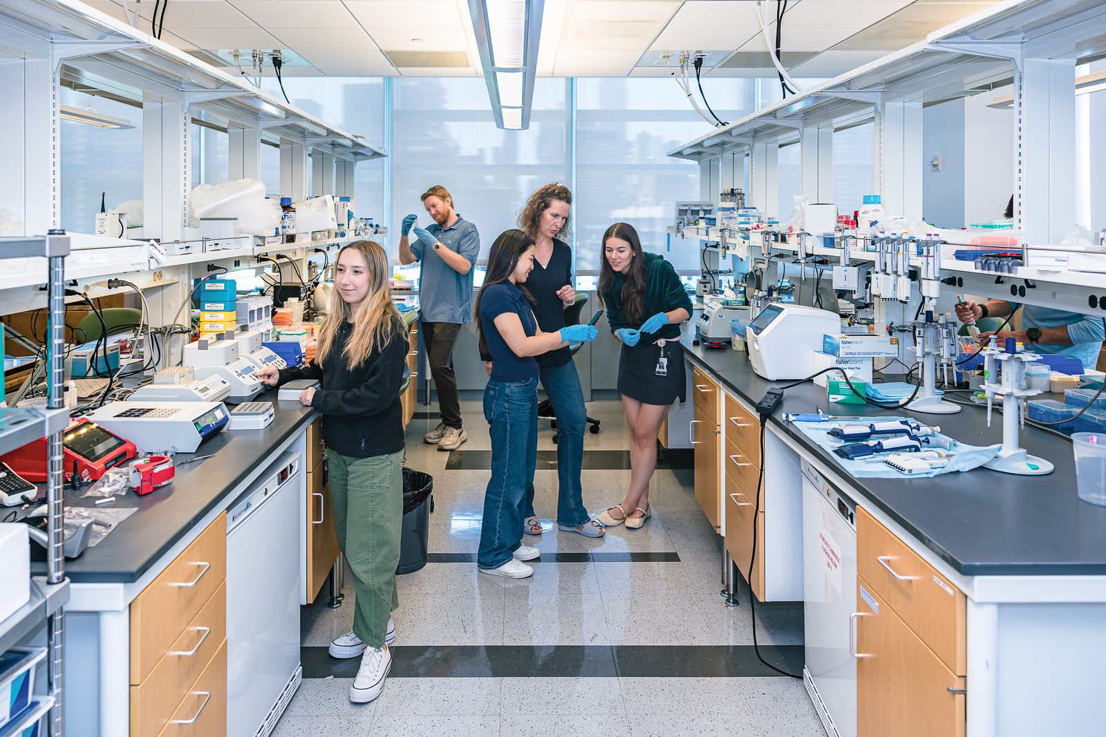 Researchers at work in a bright NYU Langone lab, one checking a sample with colleagues