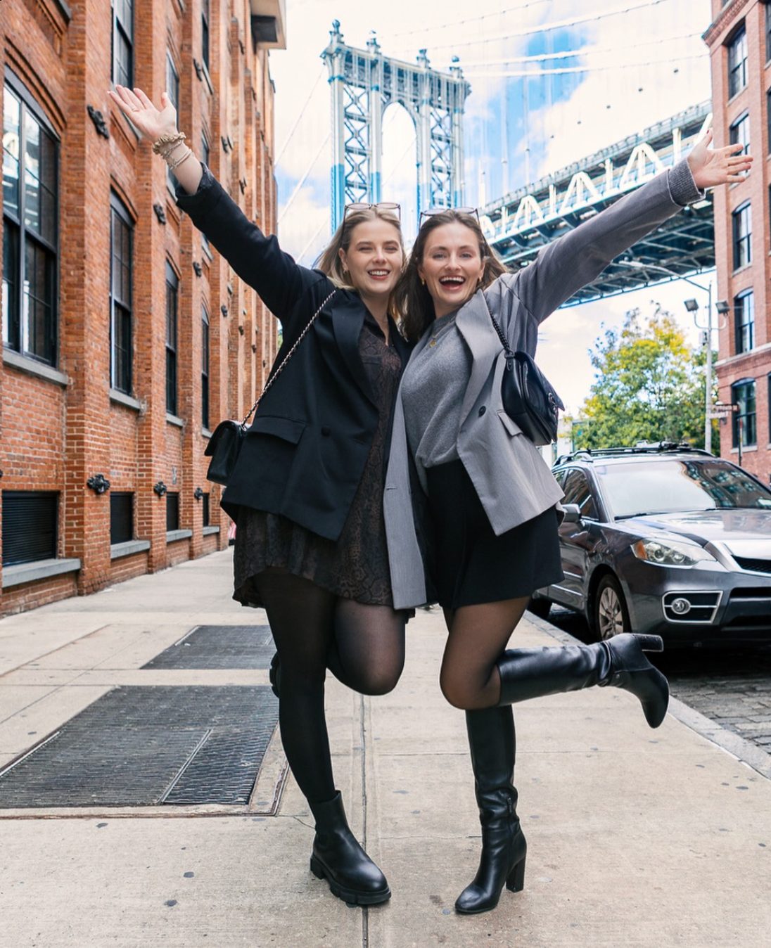 Two friends with arms raised on a Dumbo street, the Manhattan Bridge behind them