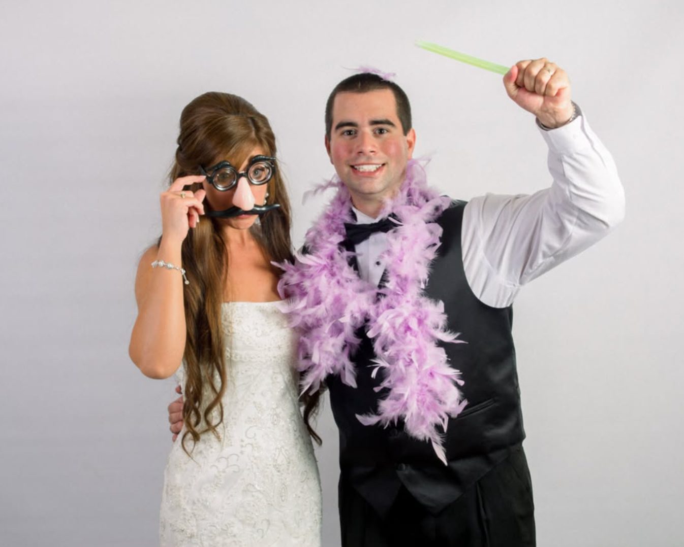 Bride and groom clowning in a wedding photo booth with novelty glasses and a feather boa